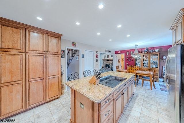 kitchen featuring light stone countertops, black electric cooktop, a center island, stainless steel refrigerator, and hanging light fixtures