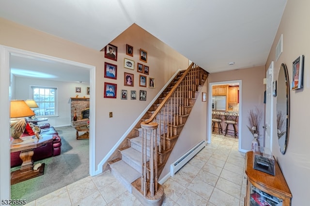 stairs with carpet flooring, a stone fireplace, and a baseboard heating unit