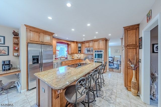 kitchen featuring backsplash, a breakfast bar area, light stone countertops, a kitchen island, and stainless steel appliances