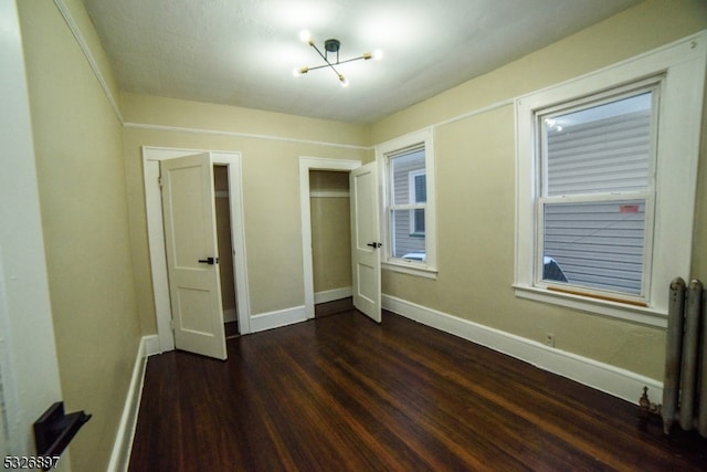 unfurnished bedroom featuring radiator heating unit, dark wood-type flooring, and a notable chandelier