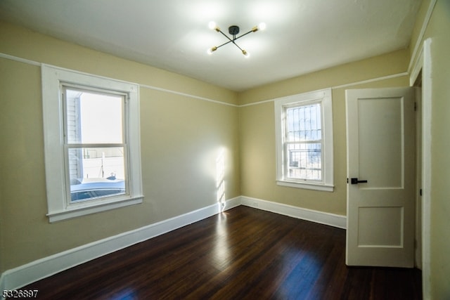 spare room featuring plenty of natural light, dark hardwood / wood-style flooring, and an inviting chandelier