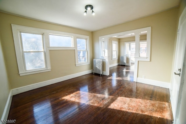 empty room with dark hardwood / wood-style floors, radiator heating unit, and decorative columns