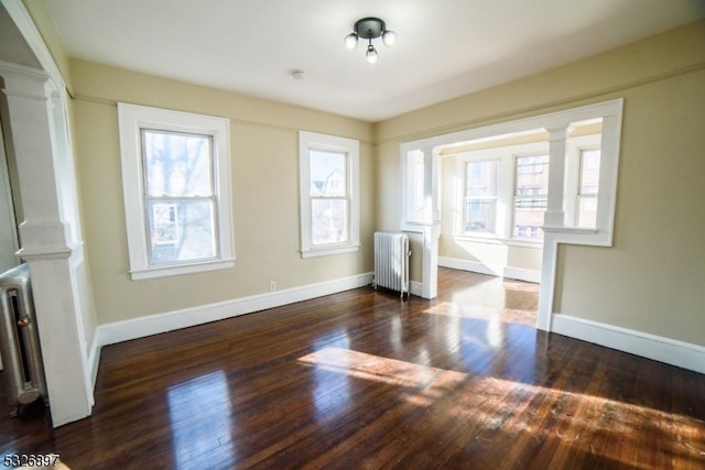 unfurnished living room featuring radiator, dark hardwood / wood-style flooring, and ornate columns