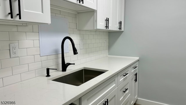 kitchen with white cabinets, decorative backsplash, light stone countertops, and sink