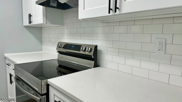 kitchen featuring stainless steel electric stove, backsplash, white cabinetry, and range hood