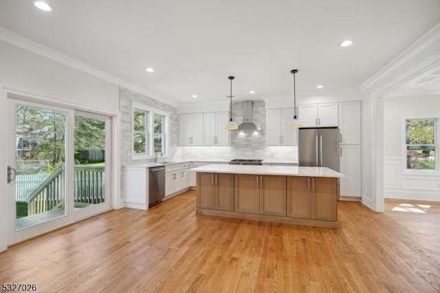 kitchen with appliances with stainless steel finishes, white cabinetry, a center island, decorative light fixtures, and wall chimney exhaust hood