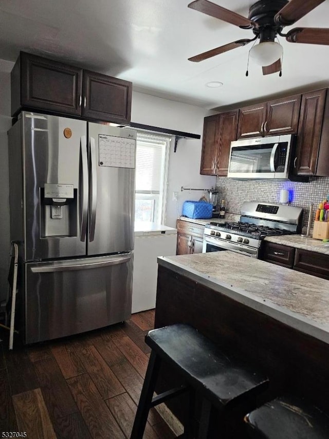 kitchen featuring stainless steel appliances, light stone counters, dark hardwood / wood-style floors, decorative backsplash, and dark brown cabinets