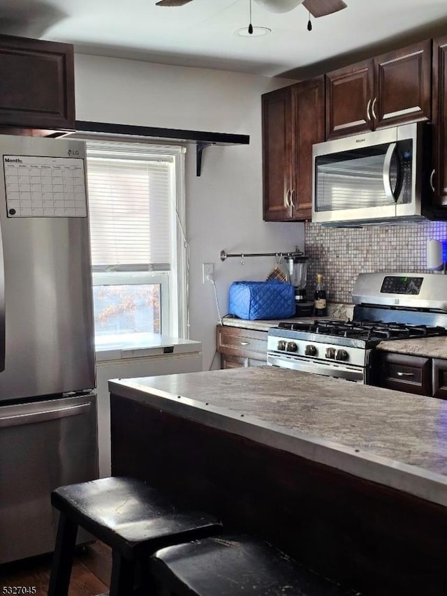 kitchen with decorative backsplash, dark brown cabinets, light stone countertops, and stainless steel appliances