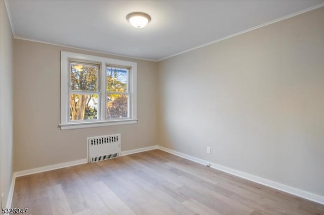 spare room featuring light wood-type flooring, radiator heating unit, and crown molding