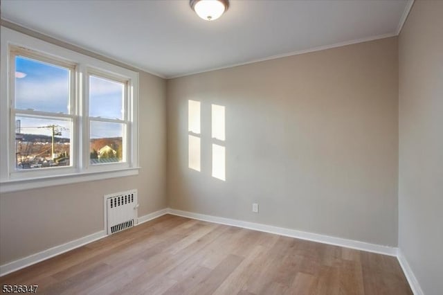 empty room featuring light wood-type flooring, radiator, and ornamental molding