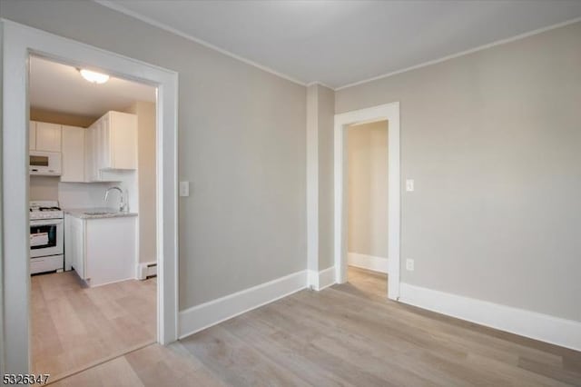 empty room with sink, baseboard heating, and light hardwood / wood-style flooring