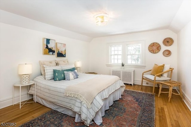 bedroom featuring radiator heating unit, wood-type flooring, and lofted ceiling