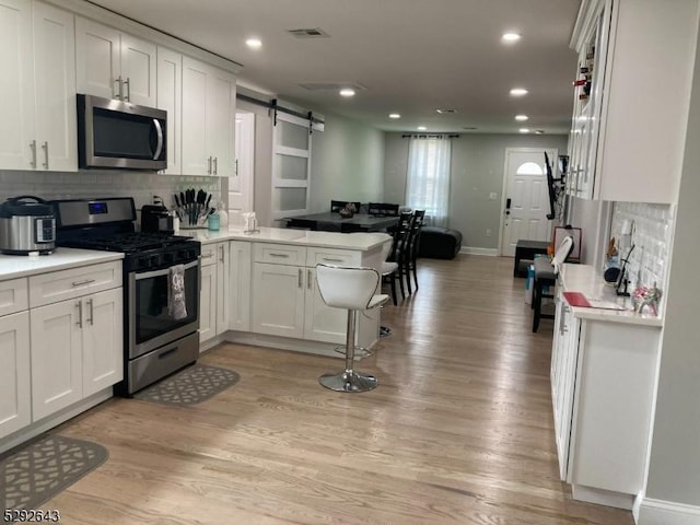 kitchen featuring a barn door, light hardwood / wood-style flooring, kitchen peninsula, white cabinets, and appliances with stainless steel finishes