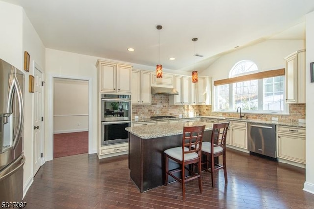 kitchen featuring light stone countertops, a center island, sink, hanging light fixtures, and appliances with stainless steel finishes