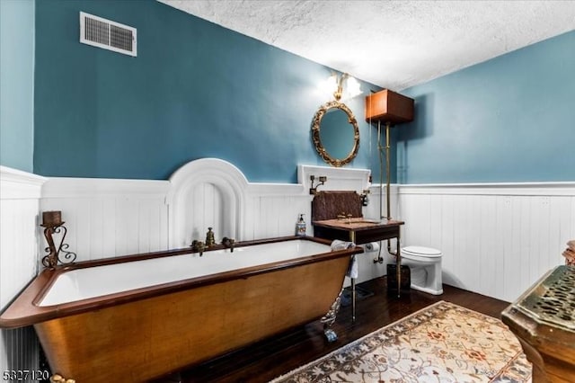 bathroom featuring a textured ceiling, hardwood / wood-style flooring, toilet, and a tub