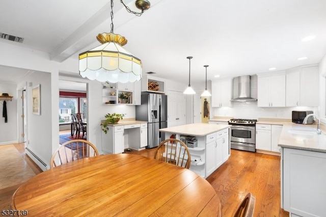 kitchen with appliances with stainless steel finishes, pendant lighting, a baseboard radiator, white cabinets, and wall chimney exhaust hood