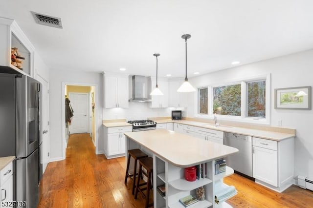 kitchen with wall chimney exhaust hood, stainless steel appliances, a kitchen island, and white cabinets