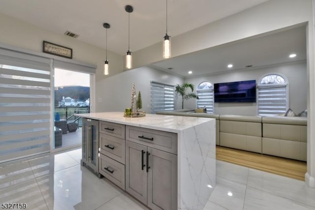 kitchen featuring light tile patterned flooring, wine cooler, decorative light fixtures, a center island, and light stone countertops