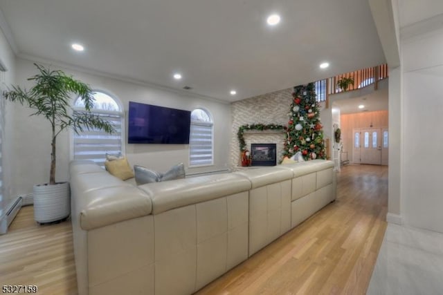 living room featuring crown molding, a stone fireplace, a baseboard heating unit, and light hardwood / wood-style floors