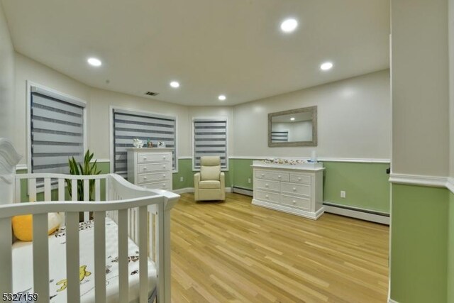 bedroom with a crib, light hardwood / wood-style flooring, and baseboard heating