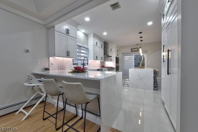 kitchen with wall chimney exhaust hood, a breakfast bar area, white cabinetry, kitchen peninsula, and pendant lighting