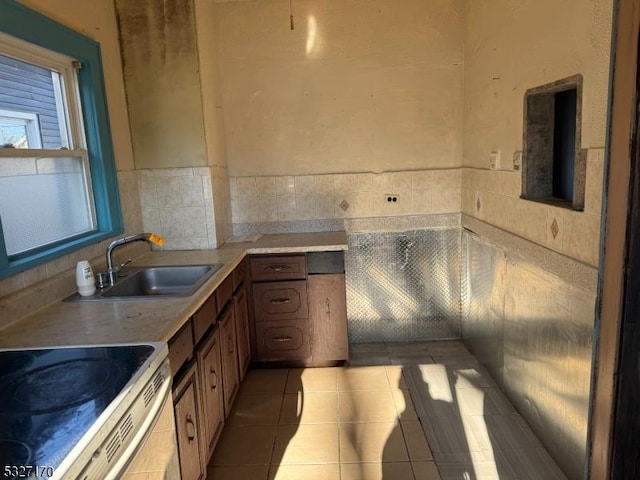 kitchen with light tile patterned floors, white range with electric stovetop, brown cabinetry, light countertops, and a sink