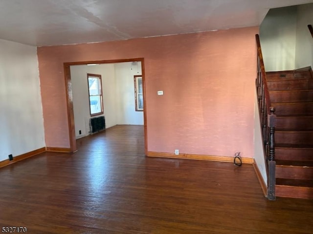 empty room with radiator, baseboards, stairway, and wood finished floors