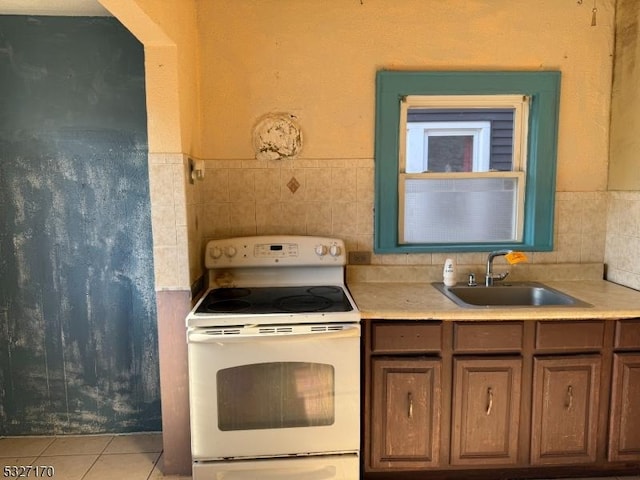 kitchen with white electric range oven, light tile patterned floors, light countertops, and a sink