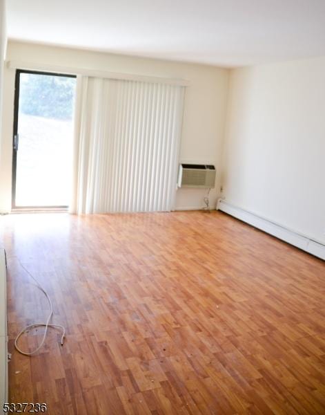 spare room featuring a wall mounted air conditioner, wood-type flooring, and a baseboard heating unit