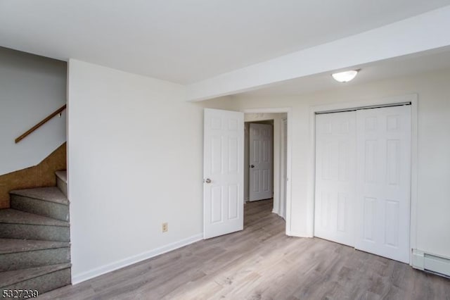 basement with light wood-type flooring and a baseboard heating unit