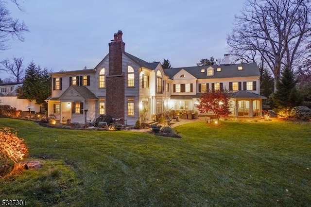 back house at dusk featuring a lawn and a patio