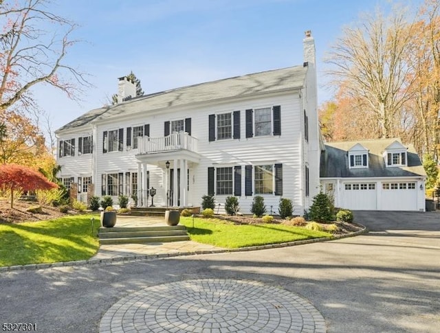 colonial house featuring a balcony, a front lawn, and a garage