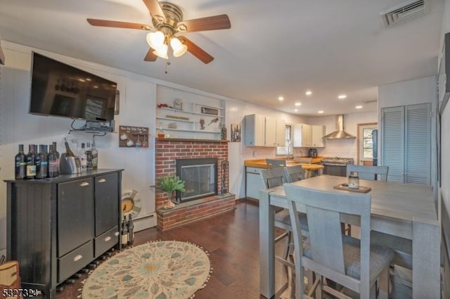 dining room featuring baseboard heating, ceiling fan, dark wood-type flooring, and a brick fireplace