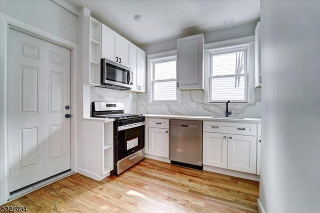 kitchen featuring sink, tasteful backsplash, light hardwood / wood-style floors, white cabinetry, and stainless steel appliances
