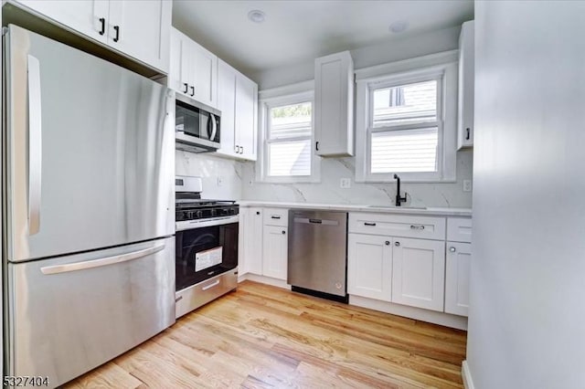 kitchen with sink, light hardwood / wood-style flooring, decorative backsplash, white cabinets, and appliances with stainless steel finishes
