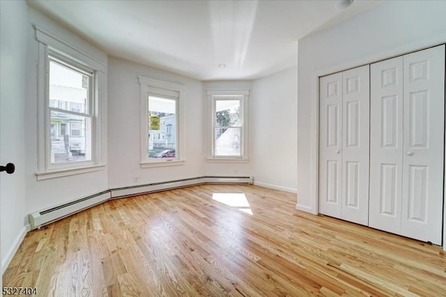unfurnished bedroom with baseboard heating, light hardwood / wood-style flooring, and multiple windows