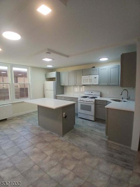 kitchen with gray cabinets, a kitchen island, white appliances, and sink