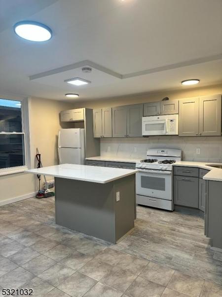 kitchen featuring white appliances, a kitchen island, and gray cabinetry