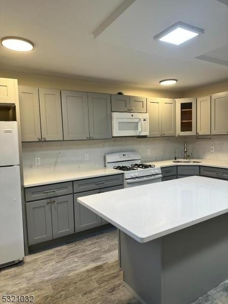 kitchen with gray cabinetry, light hardwood / wood-style floors, white appliances, and sink