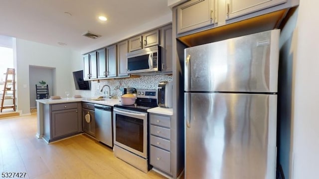 kitchen featuring kitchen peninsula, appliances with stainless steel finishes, tasteful backsplash, sink, and light hardwood / wood-style floors