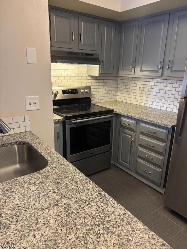 kitchen with light stone counters, decorative backsplash, gray cabinets, appliances with stainless steel finishes, and sink