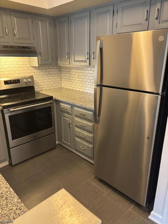 kitchen with gray cabinets, stainless steel appliances, backsplash, and light stone countertops