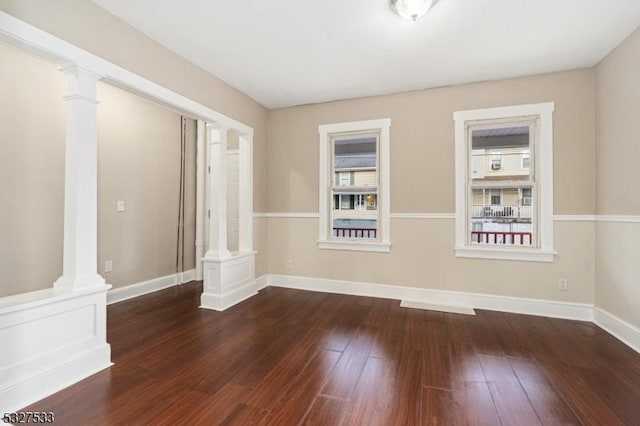 spare room featuring ornate columns and dark wood-type flooring