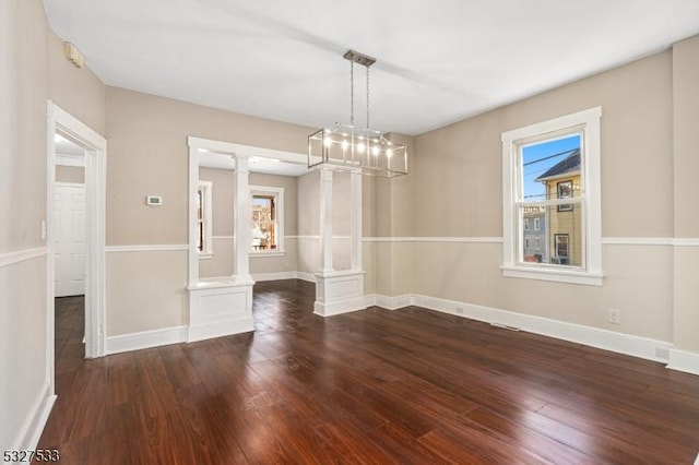 unfurnished dining area featuring a notable chandelier, dark hardwood / wood-style floors, and decorative columns