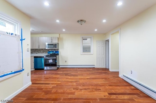 kitchen featuring backsplash, a baseboard radiator, light wood-type flooring, and appliances with stainless steel finishes