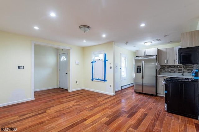 kitchen featuring decorative backsplash, stainless steel fridge, a baseboard heating unit, sink, and hardwood / wood-style flooring