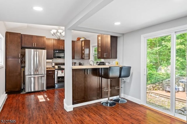 kitchen featuring kitchen peninsula, stainless steel appliances, a notable chandelier, dark hardwood / wood-style floors, and a breakfast bar area