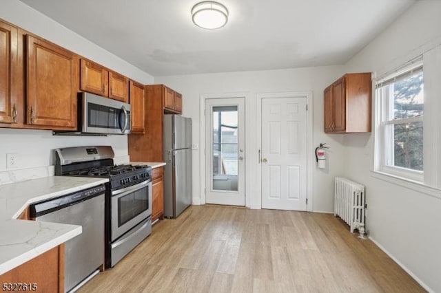 kitchen with light stone countertops, appliances with stainless steel finishes, light wood-type flooring, and radiator