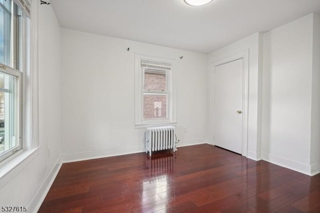 unfurnished room with radiator, plenty of natural light, and dark hardwood / wood-style flooring