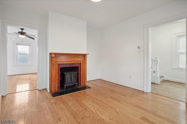 unfurnished living room with a wood stove, ceiling fan, and light wood-type flooring